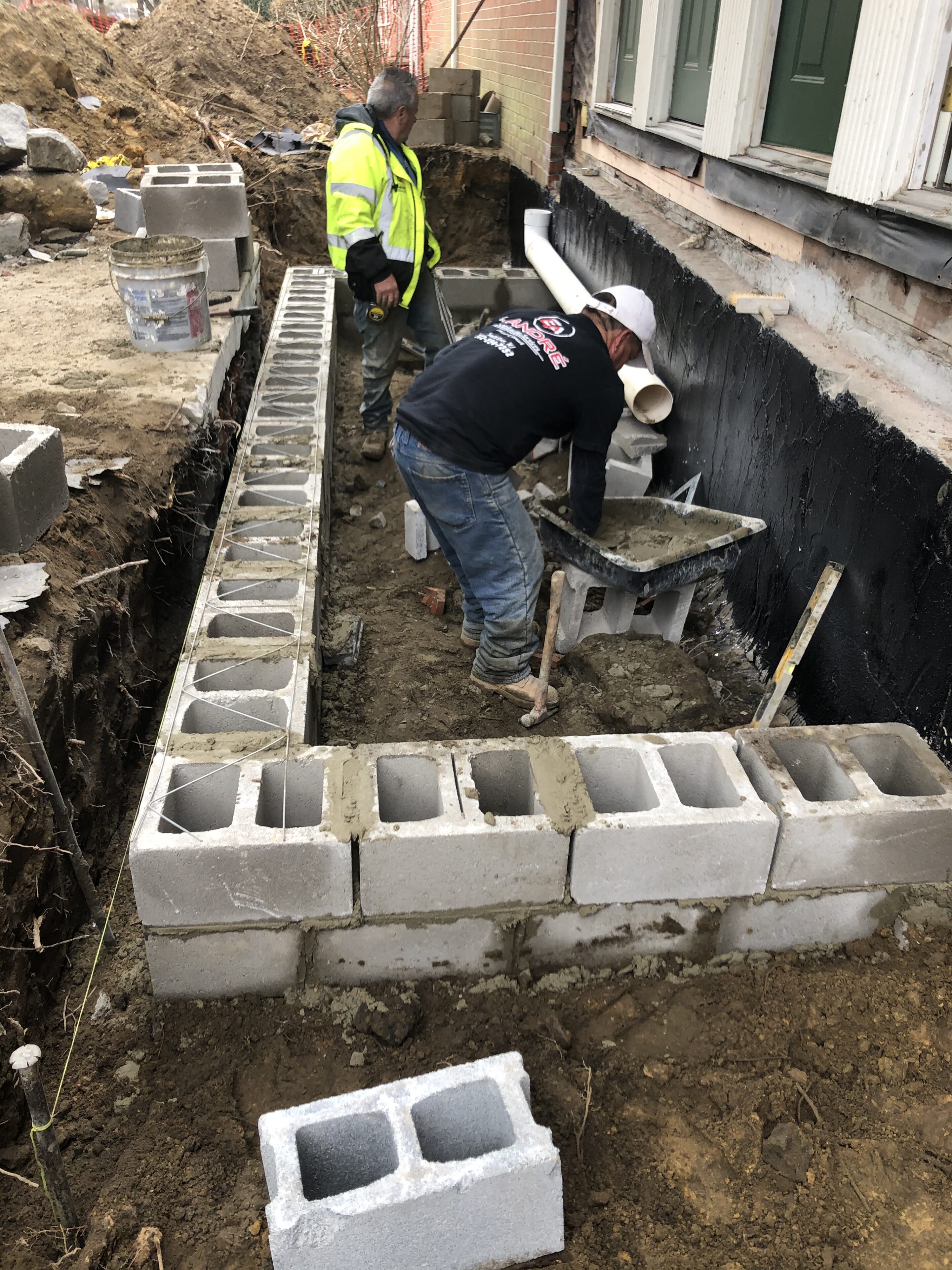 Two men working on a cinder block wall in front of a house