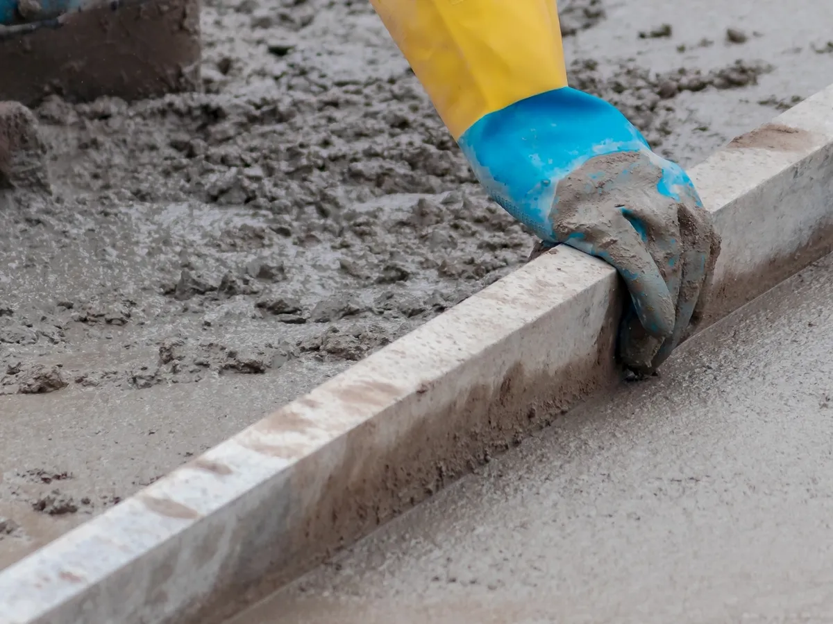Person wearing gloves and using a trowel to spread concrete on a concrete slab