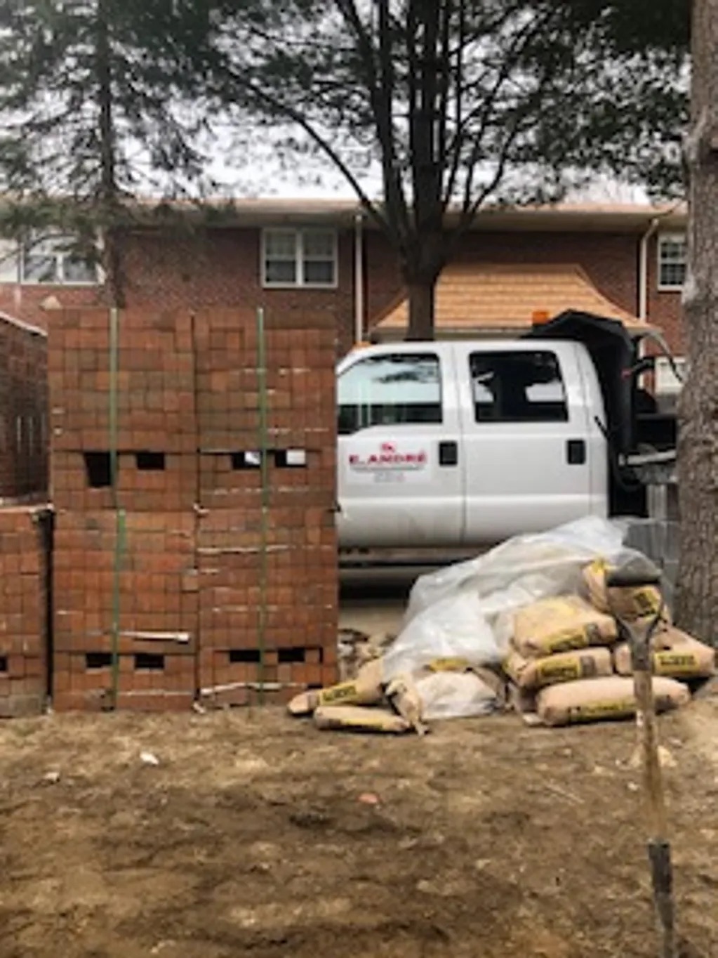 White van parked in front of a brick wall, with sandbags on the ground and trees