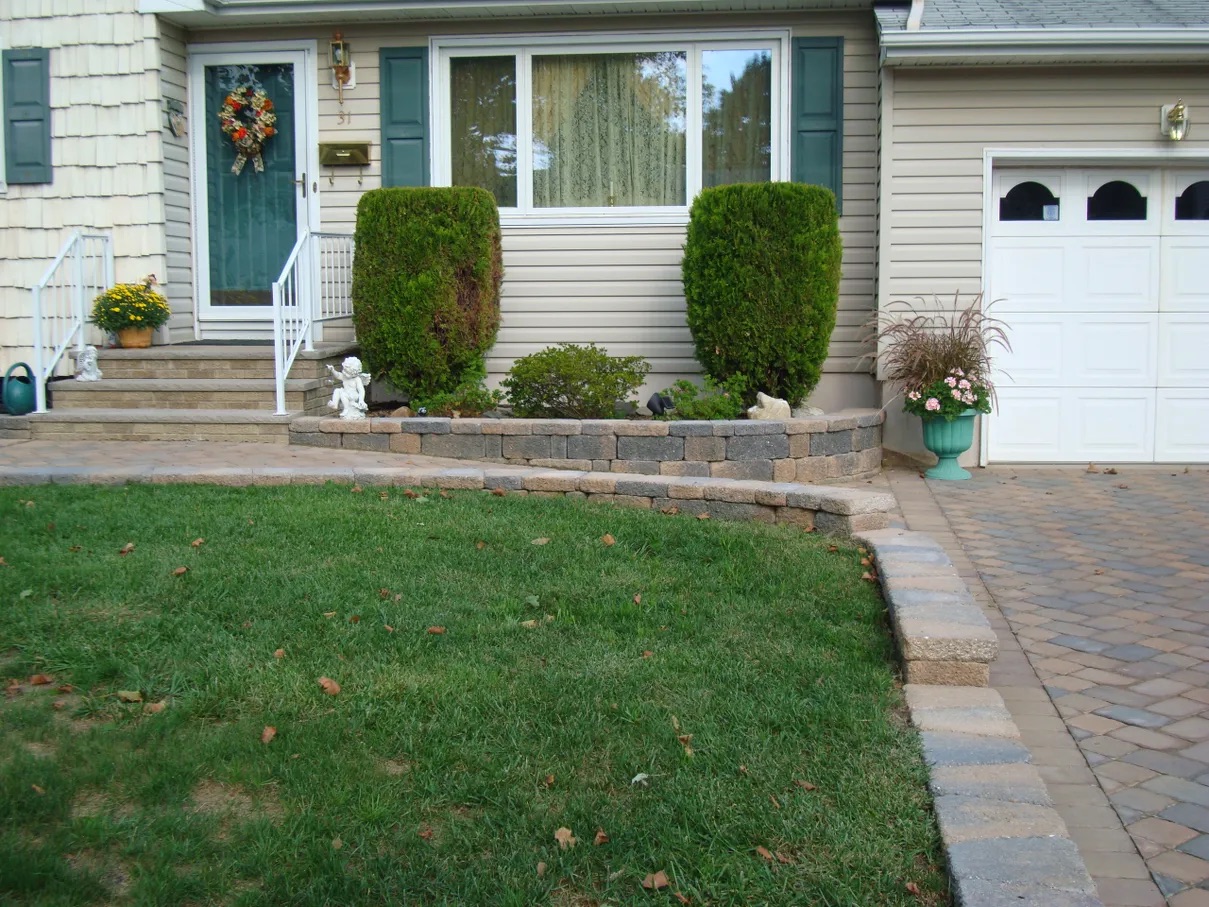 House with a brick walkway up to the front door, surrounded by grass, plants, stairs, railings, flower pots